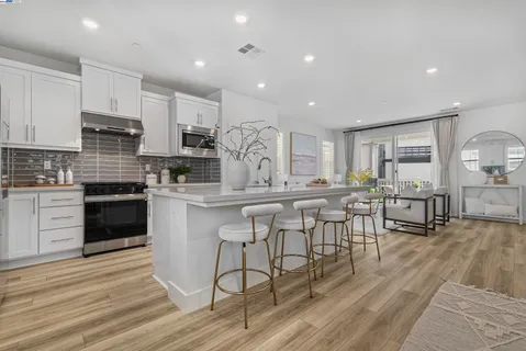 a kitchen with stainless steel appliances granite countertop a stove a sink a refrigerator and white cabinets with wooden floor