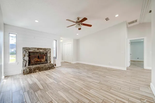 an empty room with wooden floor a ceiling fan a fireplace and windows