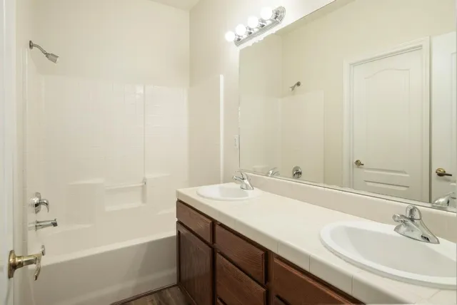 a bathroom with a tub sink vanity granite and shower