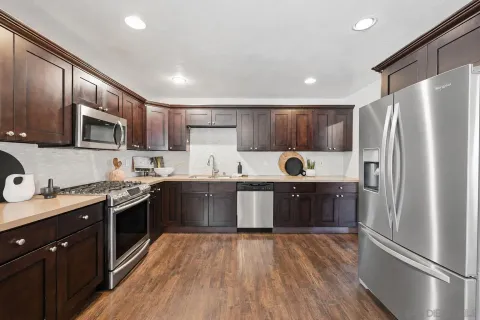 a kitchen with kitchen island granite countertop wooden floors stainless steel appliances a sink and a refrigerator
