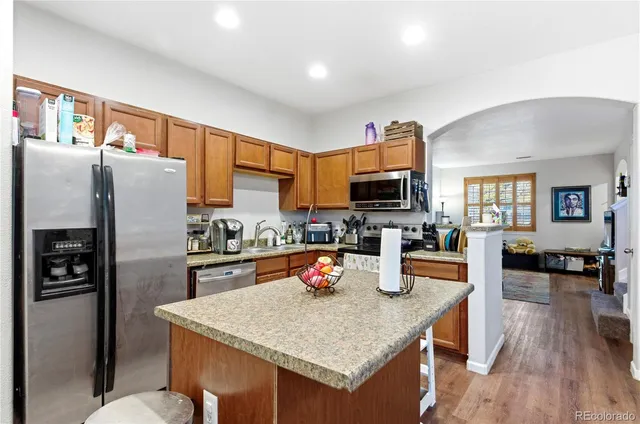 a kitchen with stainless steel appliances granite countertop a refrigerator a stove top oven a sink dishwasher and wooden cabinets with wooden floor