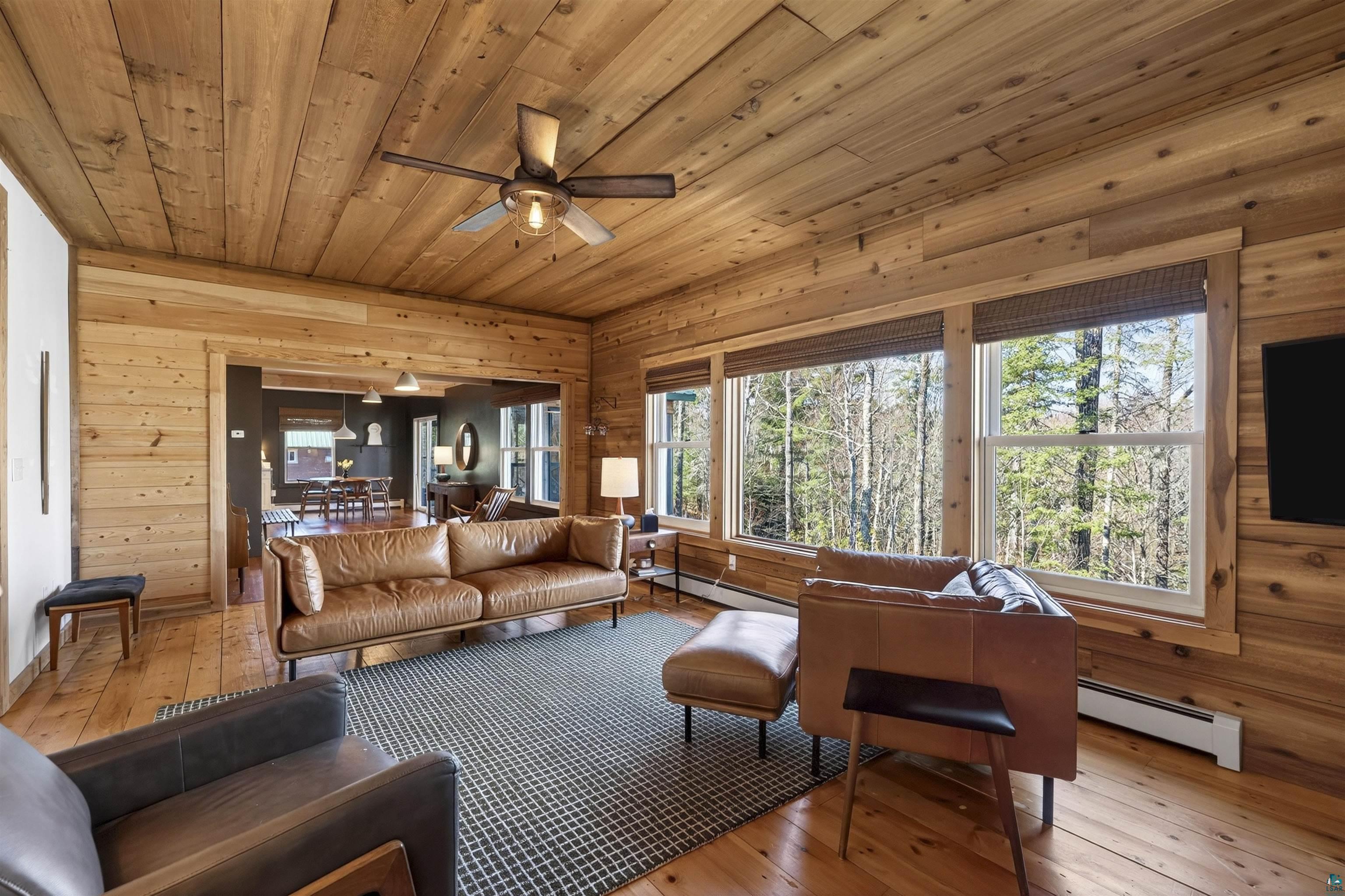 13885 Park Road Brule, WI 54820 - Photo 15 of 41 Living room featuring extensive wood paneling on walls and ceiling, wood-finish flooring, a ceiling fan with integrated lighting, and multiple large windows
