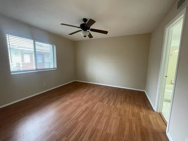 an empty room with wooden floor fan and windows
