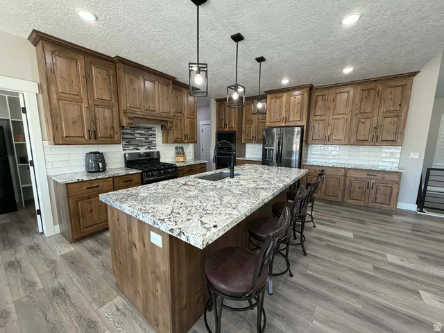 2350 North 1075 West Helper, UT 84526 - Photo 9 of 49 Kitchen featuring a textured ceiling, backsplash, brown cabinetry, a kitchen bar, and recessed lighting
