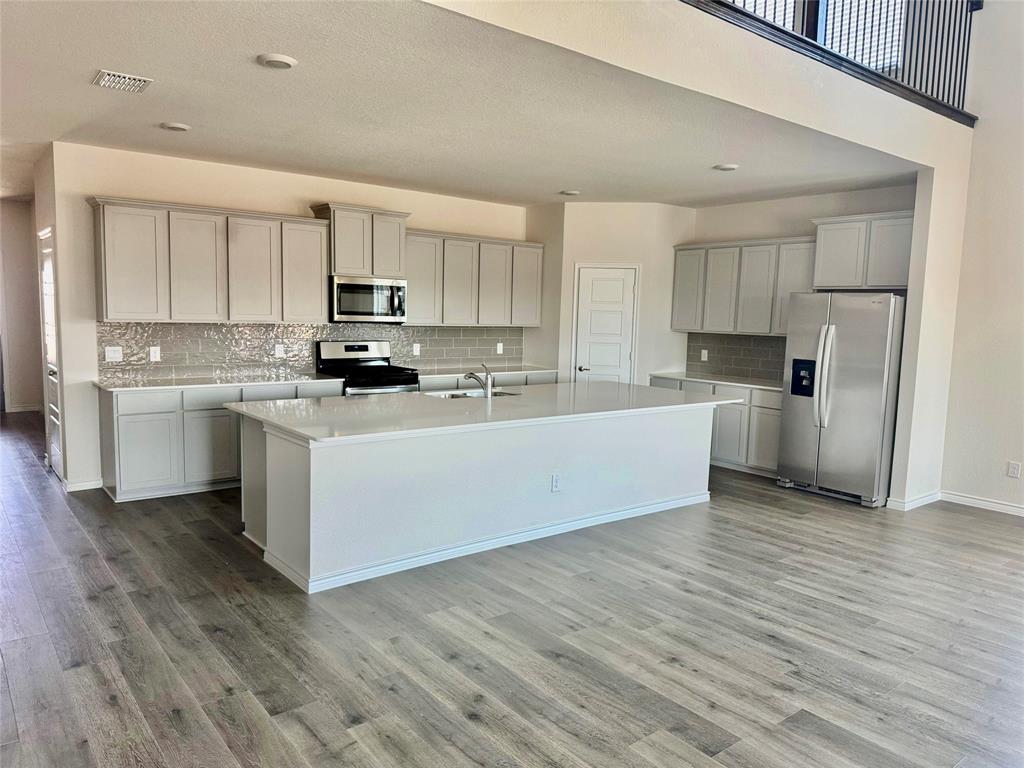 2408 Grapevine Way Celina, TX 75009 - Photo 2 of 20 Kitchen featuring decorative backsplash, stainless steel appliances, an island with sink, light wood-style flooring, and light stone countertops