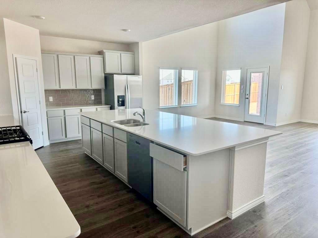 2408 Grapevine Way Celina, TX 75009 - Photo 3 of 20 Kitchen featuring stainless steel appliances, an island with sink, dark wood-style flooring, backsplash, and white cabinets