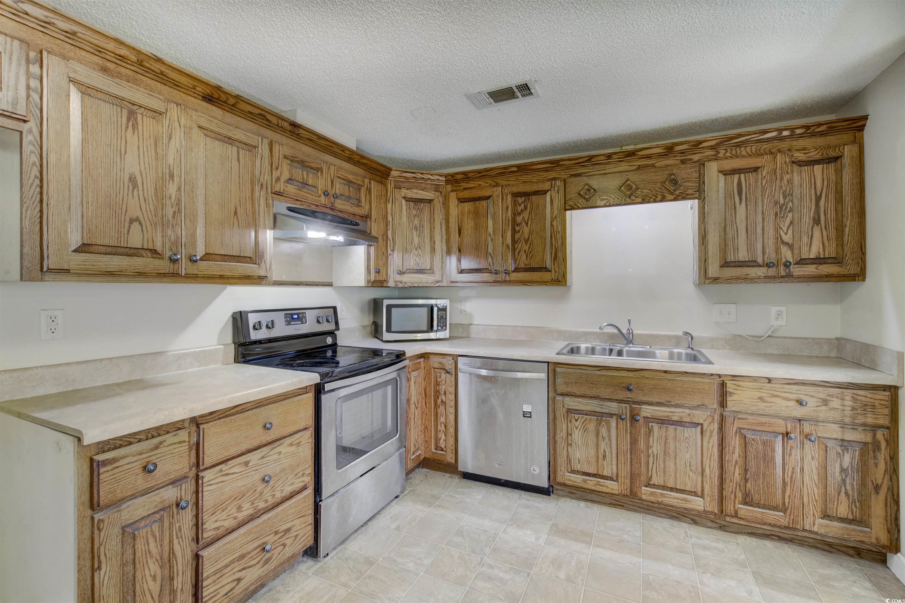 2080 Highway 90 Conway, SC 29526 - Photo 8 of 29 Kitchen featuring appliances with stainless steel finishes, light countertops, under cabinet range hood, brown cabinets, and a textured ceiling