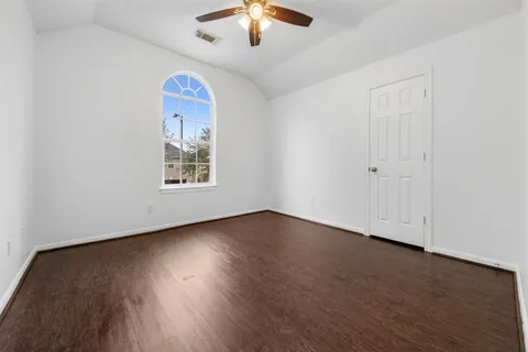 an empty room with wooden floor chandelier fan and windows
