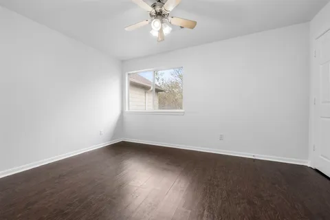 an empty room with wooden floor ceiling fan and windows