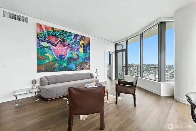 a living room with couches a coffee table and kitchen view with wooden floor