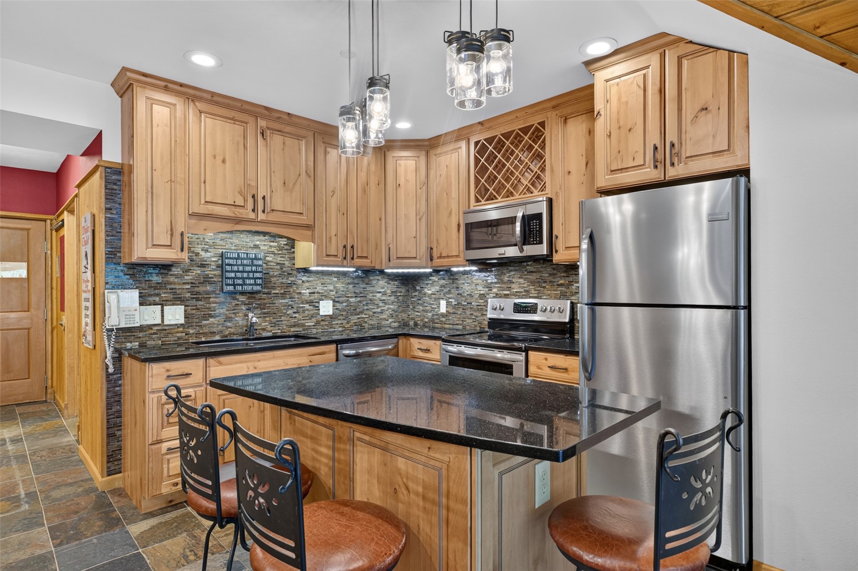 Wood cabinetry, black stone countertops, stainless steel appliances, stacked stone backsplash, and recessed lighting
