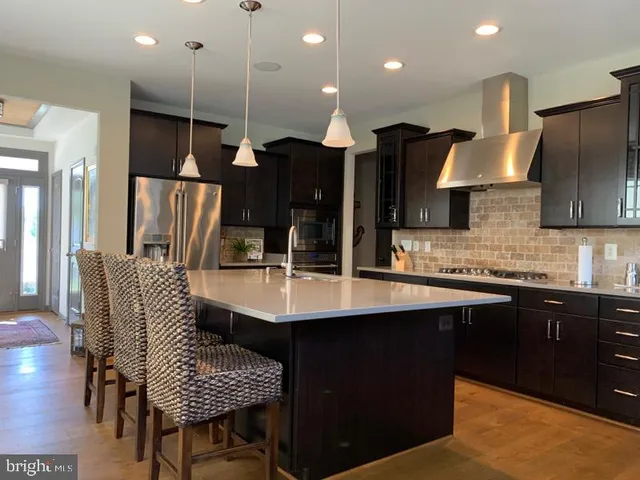 a kitchen with stainless steel appliances kitchen island granite countertop a sink a stove a refrigerator and chairs