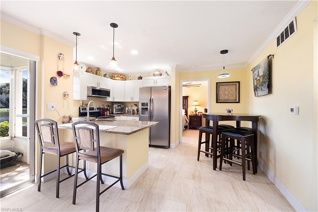 2008 Rookery Bay Drive, Unit 1102 Naples, FL 34114 - Photo 4 of 34 a kitchen with stainless steel appliances kitchen island granite countertop a table chairs and a refrigerator