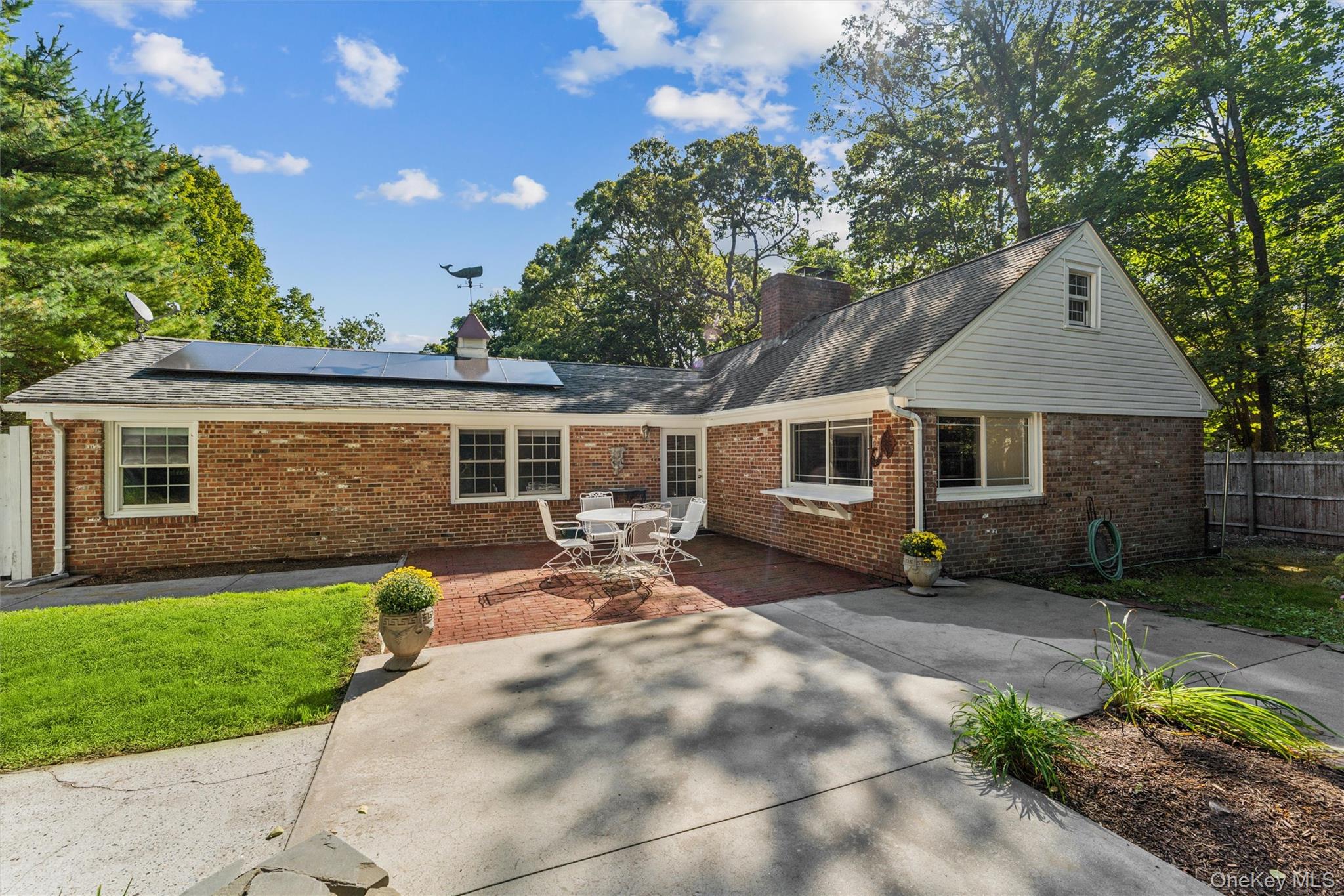 29 Squiretown Road, Unit D Hampton Bays, NY 11946 - Photo 2 of 16 Brick exterior home with solar panels, a gabled roofline, and a cupola with a weather vane