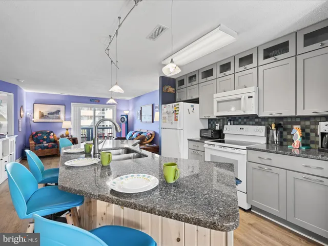 a kitchen with stainless steel appliances granite countertop a refrigerator a sink dishwasher a dining table and chairs with wooden floor