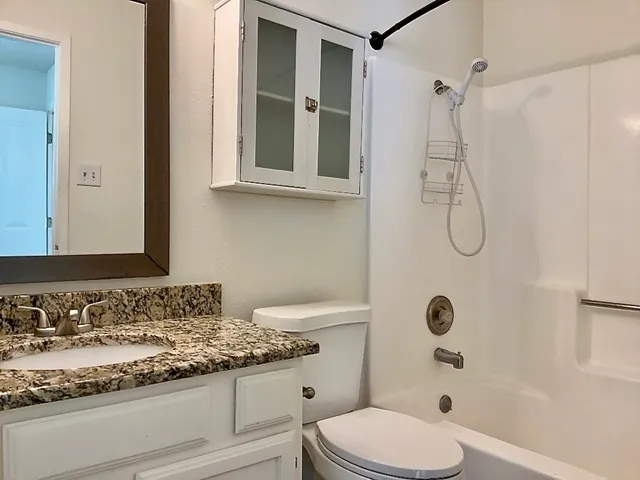 a bathroom with a granite countertop sink a toilet and shower