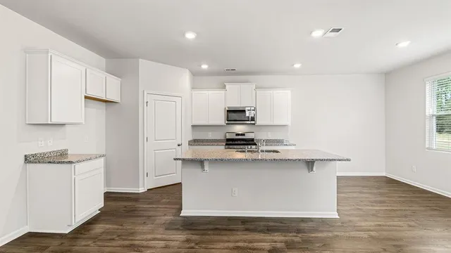 a kitchen with stainless steel appliances granite countertop a stove top oven a sink a refrigerator and white cabinets with wooden floor