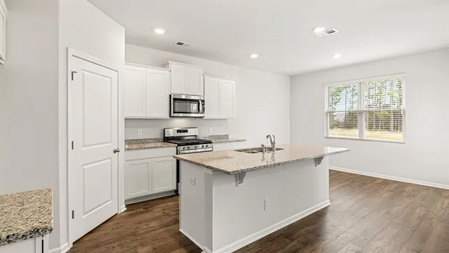 a kitchen with stainless steel appliances granite countertop a sink stove refrigerator and white cabinets with wooden floor