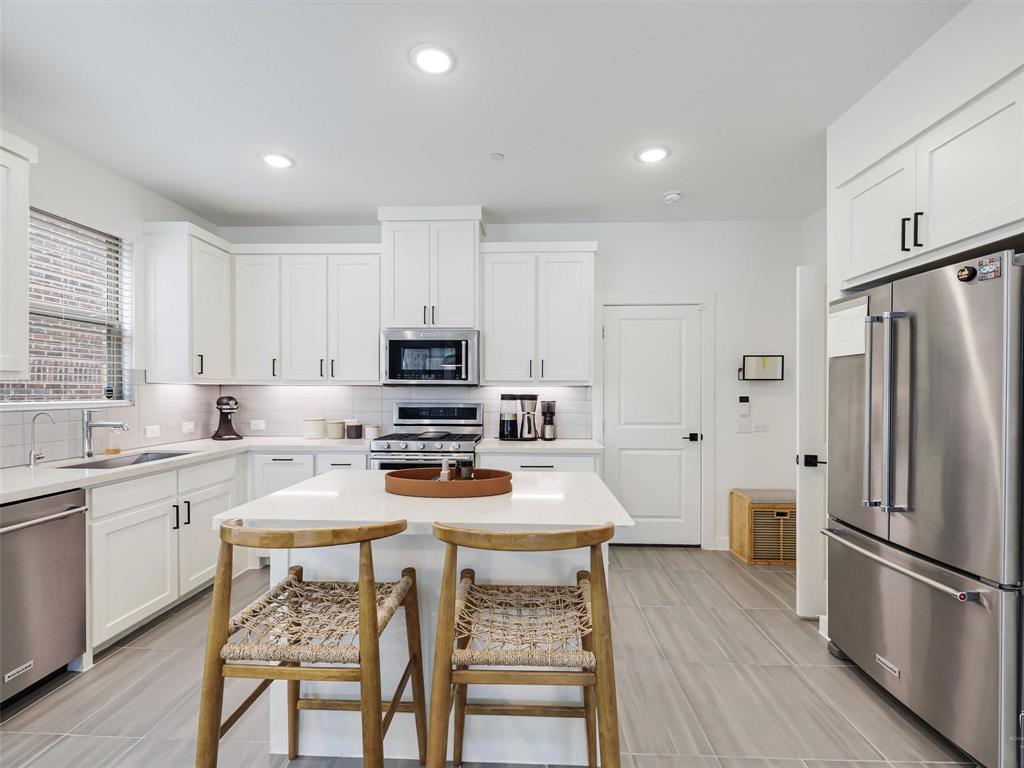 5912 Ridgeline Drive McKinney, TX 75070 - Photo 8 of 22 a kitchen with stainless steel appliances a stove a sink refrigerator and white cabinets with wooden floor