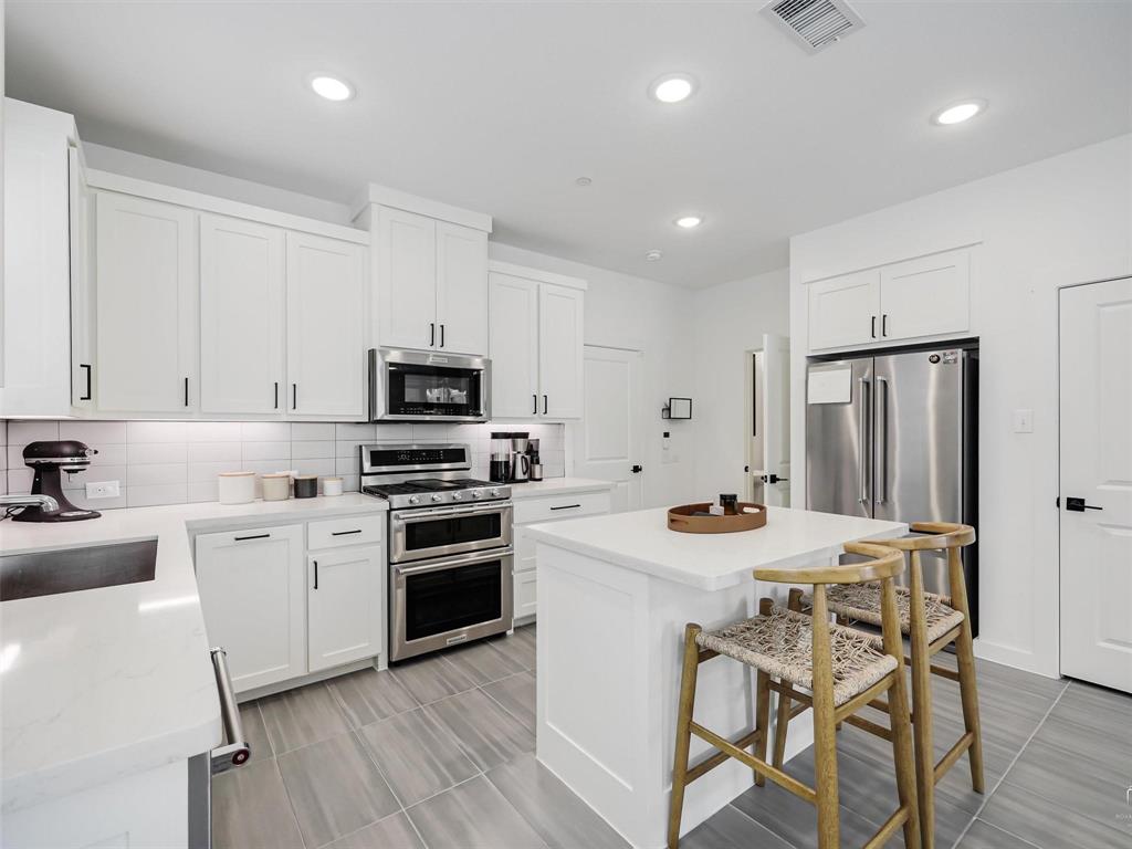 5912 Ridgeline Drive McKinney, TX 75070 - Photo 9 of 22 a kitchen with stainless steel appliances a stove a sink a microwave a refrigerator and white cabinets with wooden floor