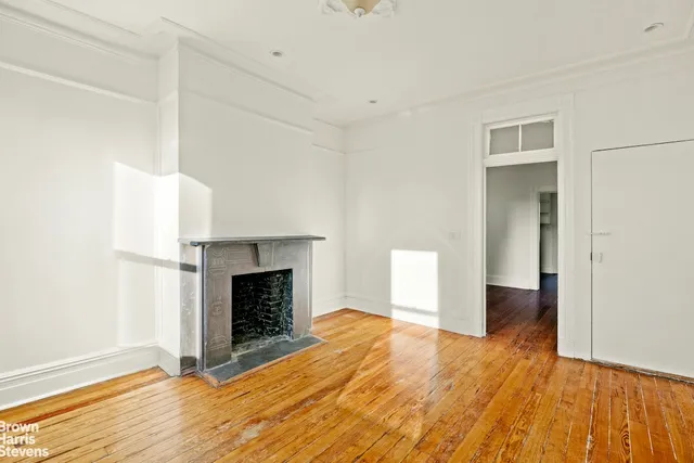 a view of an empty room with wooden floor and a fireplace
