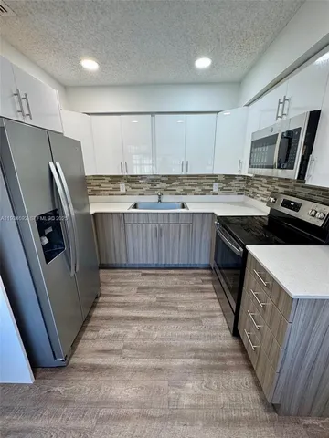 a kitchen with stainless steel appliances granite countertop a stove top oven a sink a refrigerator white cabinets and wooden floor