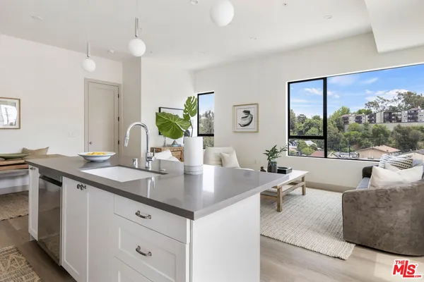 a view of living room kitchen with stainless steel appliances granite countertop a sink and white cabinets next to a window