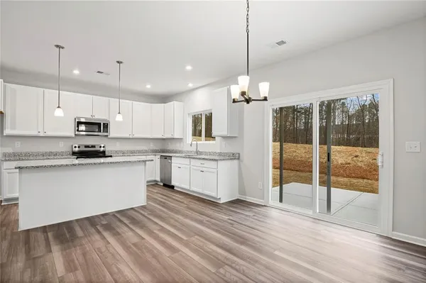 a kitchen with stainless steel appliances kitchen island granite countertop a stove a sink and white cabinets with wooden floor