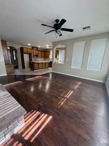 a view of an empty room with wooden floor ceiling fan and windows