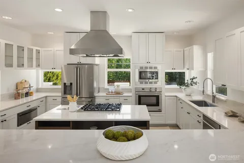 a kitchen with stainless steel appliances a sink a stove a refrigerator and white cabinets