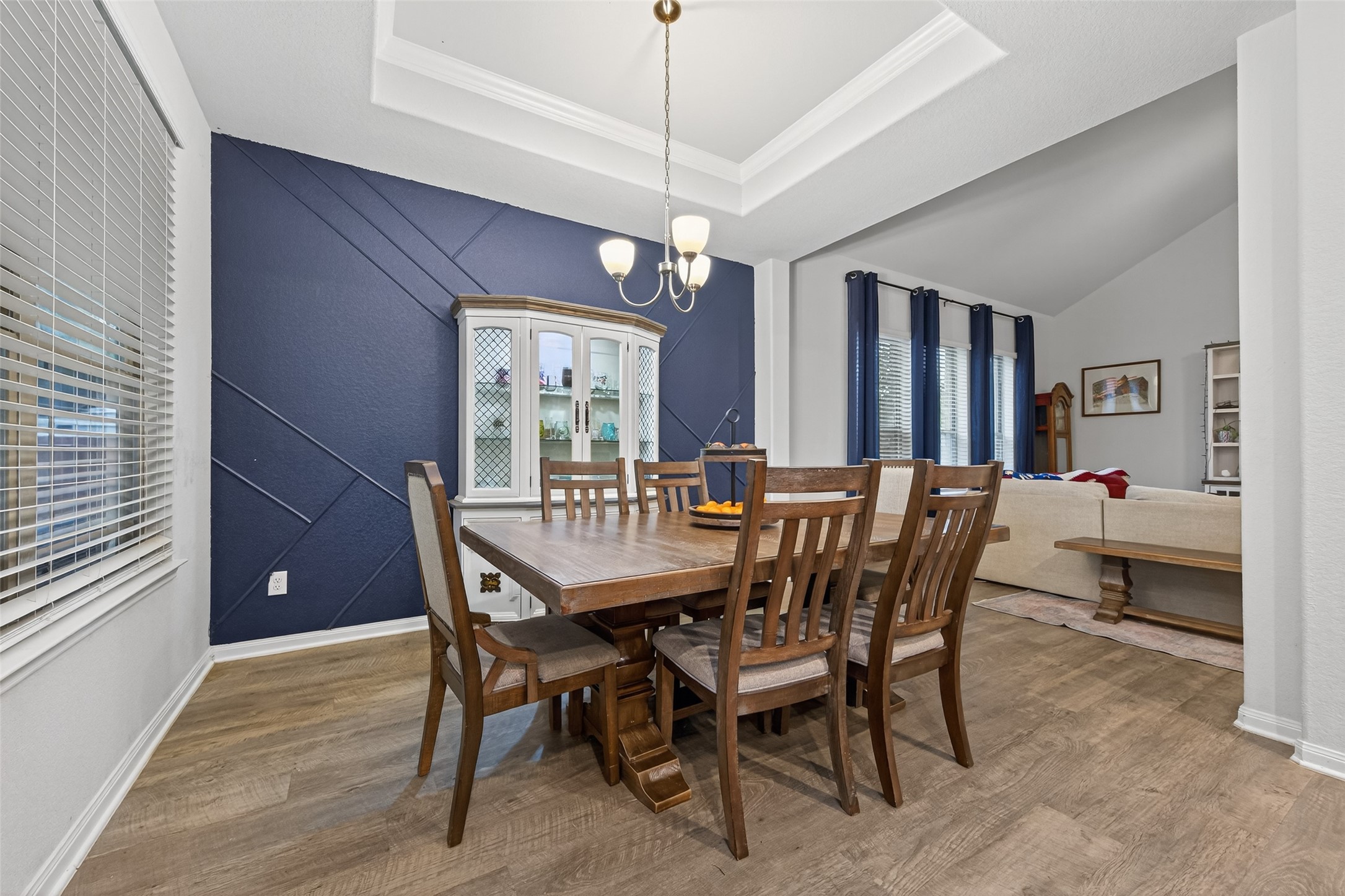 16601 Crosby Street Conroe, TX 77303 - Photo 10 of 50 Elegant dining room featuring a bold accent wall, tray ceiling, and wood-look flooring—perfect for gatherings and open to the spacious living area.