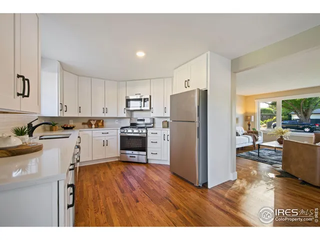 a kitchen with a refrigerator a stove top oven a sink dishwasher and white cabinets with wooden floor