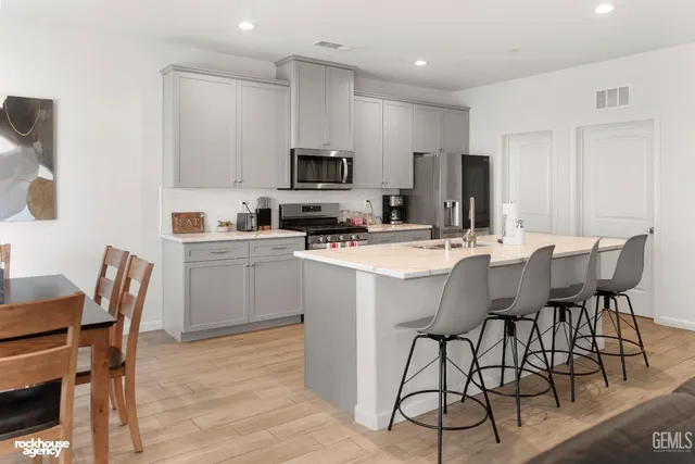 a white kitchen with stainless steel appliances granite countertop a table and chairs a refrigerator with wooden floors