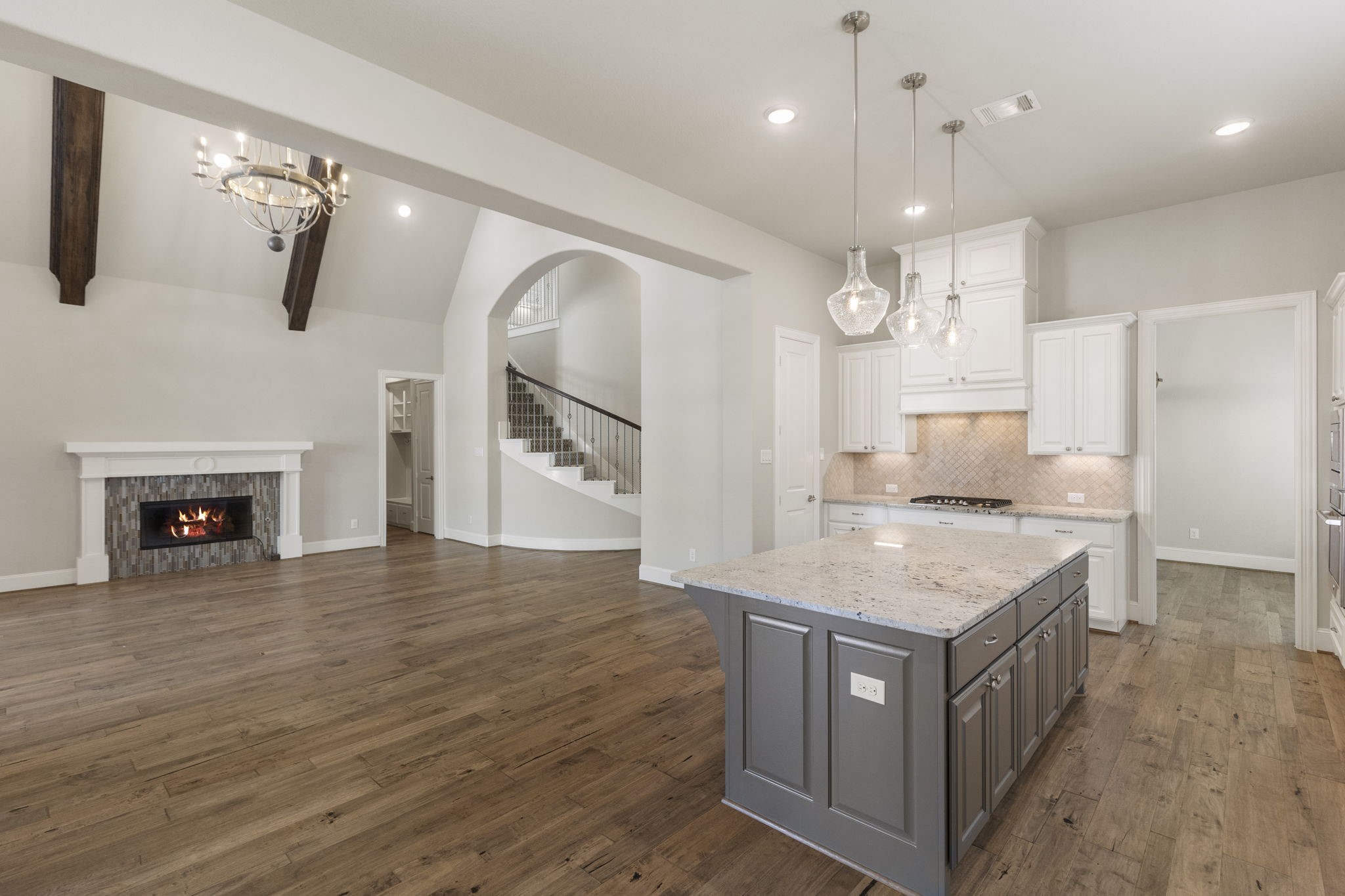 25002 Rosa Aurora Way Spring, TX 77389 - Photo 14 of 38 This spacious open-concept living area features hardwood floors, a modern kitchen with a large island, and a cozy fireplace. High ceilings, elegant light fixtures, and a sweeping staircase add a touch of luxury. Perfect for entertaining and family living.