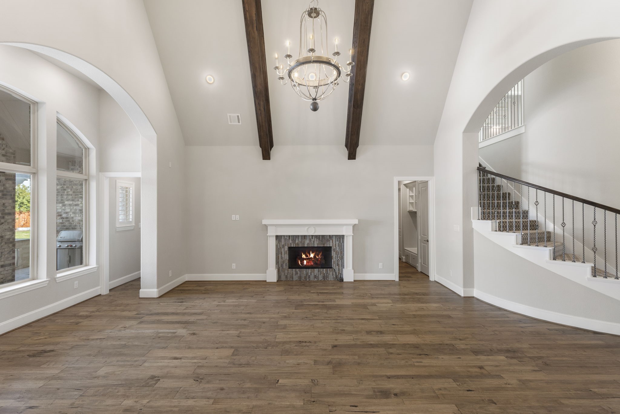 25002 Rosa Aurora Way Spring, TX 77389 - Photo 15 of 38 This spacious living room features high ceilings with exposed wooden beams, a central fireplace, and elegant chandelier. Large arched windows provide plenty of natural light, and a sweeping staircase adds a touch of luxury.