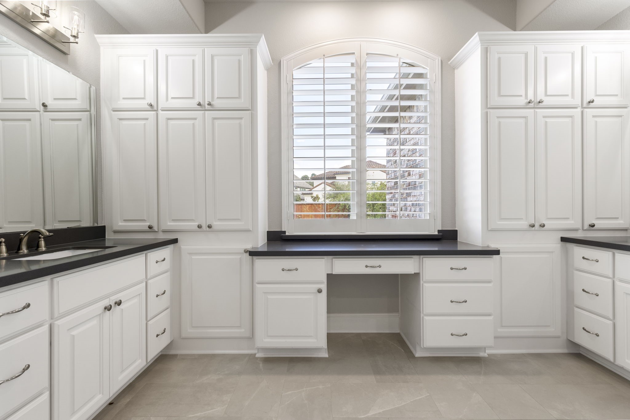 25002 Rosa Aurora Way Spring, TX 77389 - Photo 19 of 38 Elegant primary bathroom with ample white cabinetry, black countertops, and a large window with shutters. The layout is functional, featuring a built-in vanity area, and the design is bright and modern.
