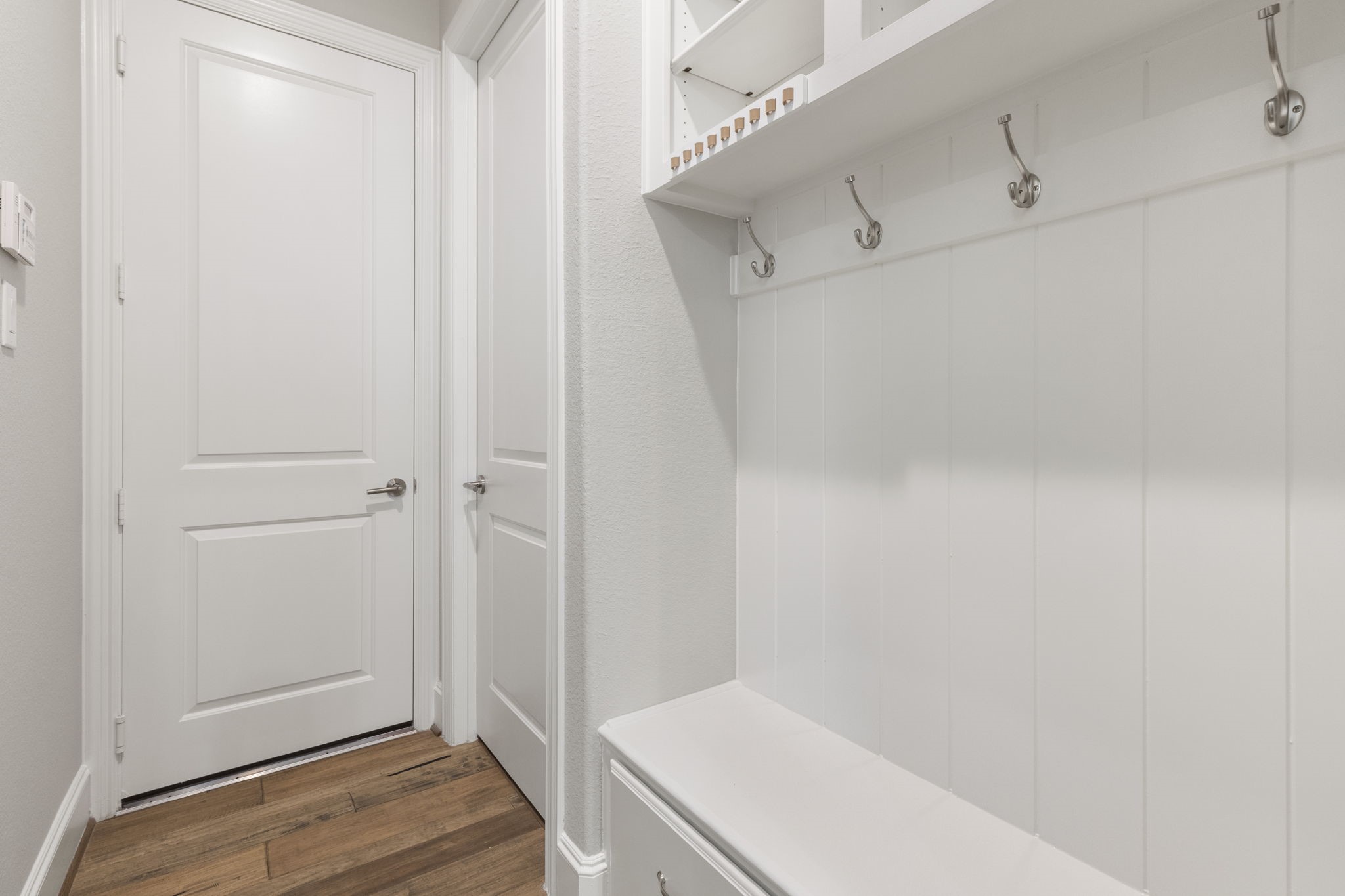 25002 Rosa Aurora Way Spring, TX 77389 - Photo 23 of 38 Bright and tidy mudroom or hallway area with white paneled walls, multiple coat hooks, and storage shelves. It features contrasting wood flooring and two white doors, creating a clean and organized entry space.