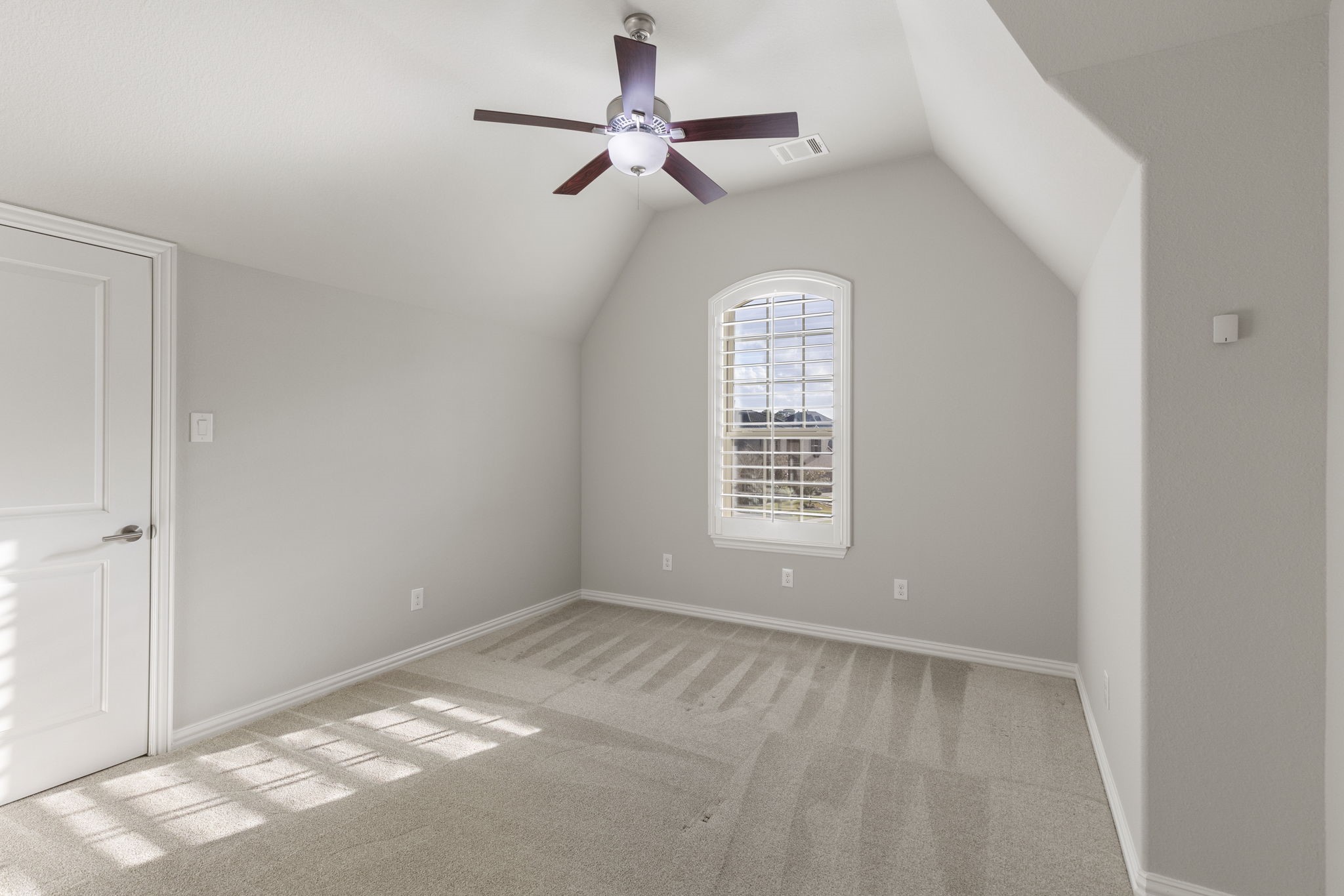 25002 Rosa Aurora Way Spring, TX 77389 - Photo 29 of 38 This room features a vaulted ceiling with a modern ceiling fan, soft gray walls, and a plush carpet. A large window with shutters allows natural light to illuminate the space.