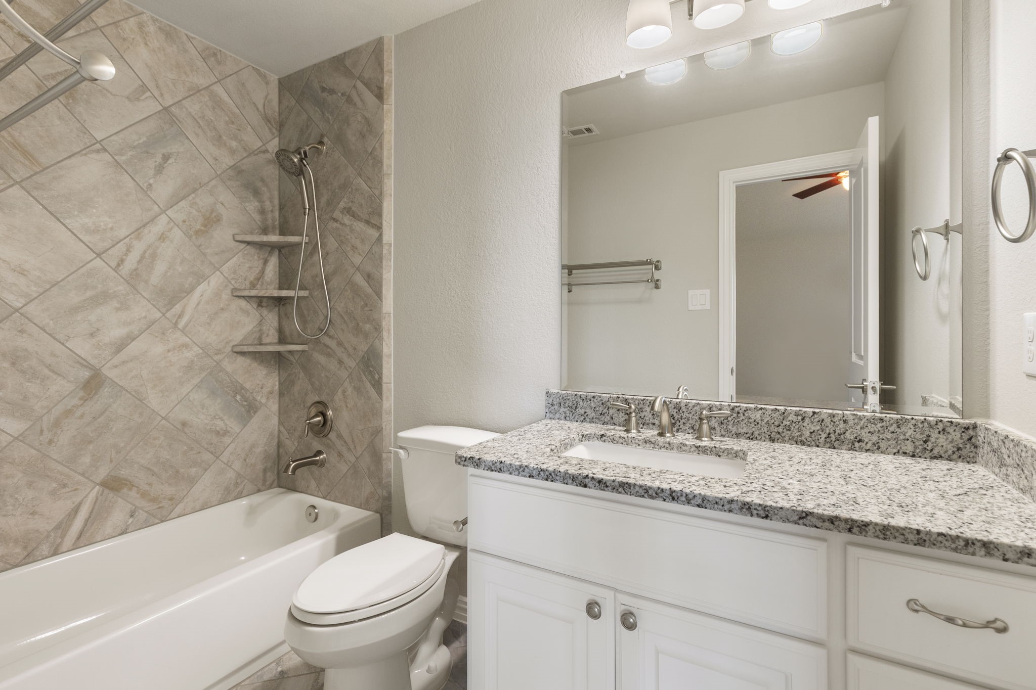 25002 Rosa Aurora Way Spring, TX 77389 - Photo 32 of 38 This bathroom features a modern design with a granite countertop, a large mirror, and bright lighting. It includes a shower-tub combo with stylish tilework and ample storage below the sink.
