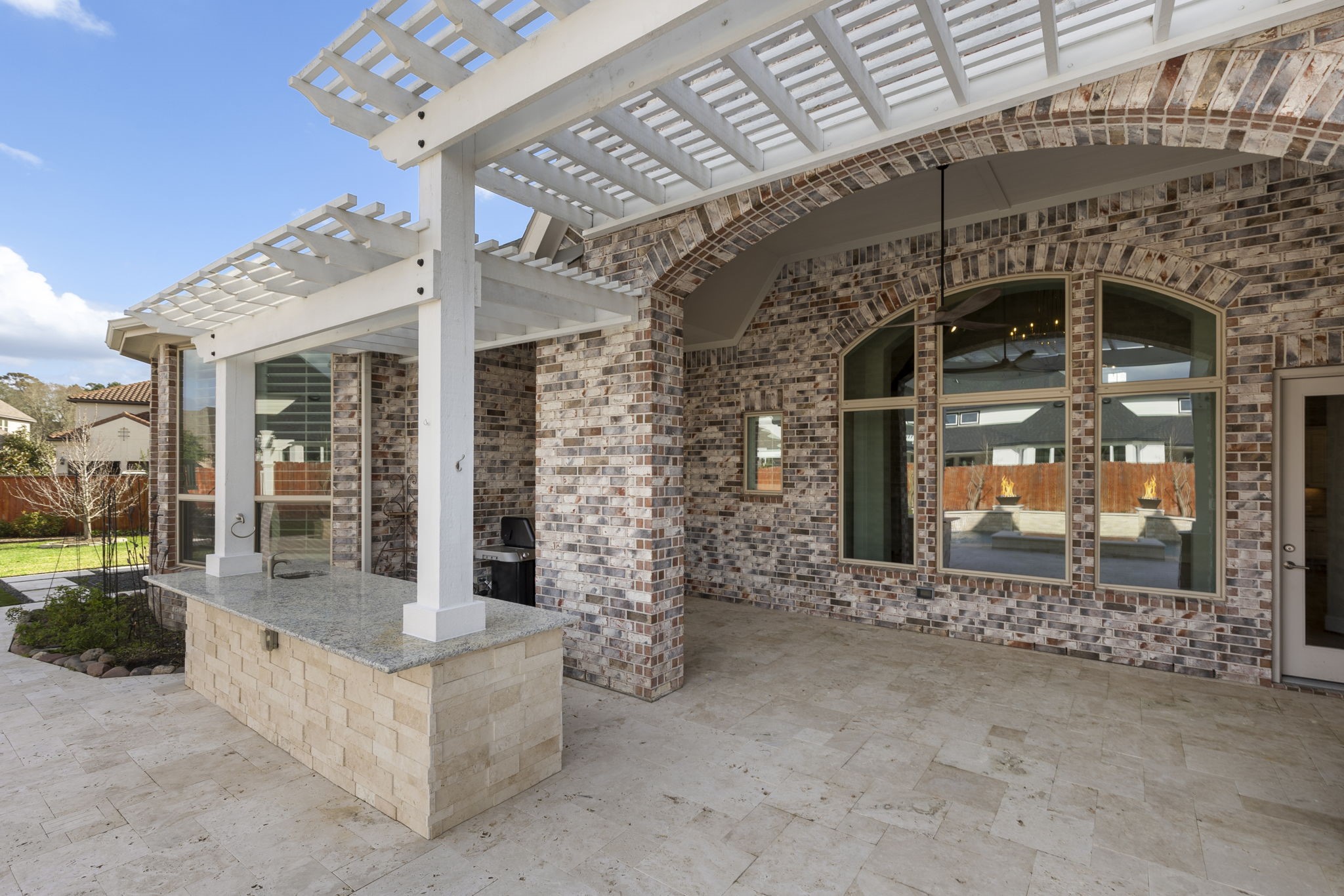 25002 Rosa Aurora Way Spring, TX 77389 - Photo 33 of 38 Spacious, covered outdoor patio with elegant brickwork and a pergola. It features a built-in countertop and sink, ideal for entertaining. Large windows enhance the space, providing a view of the landscaped backyard.