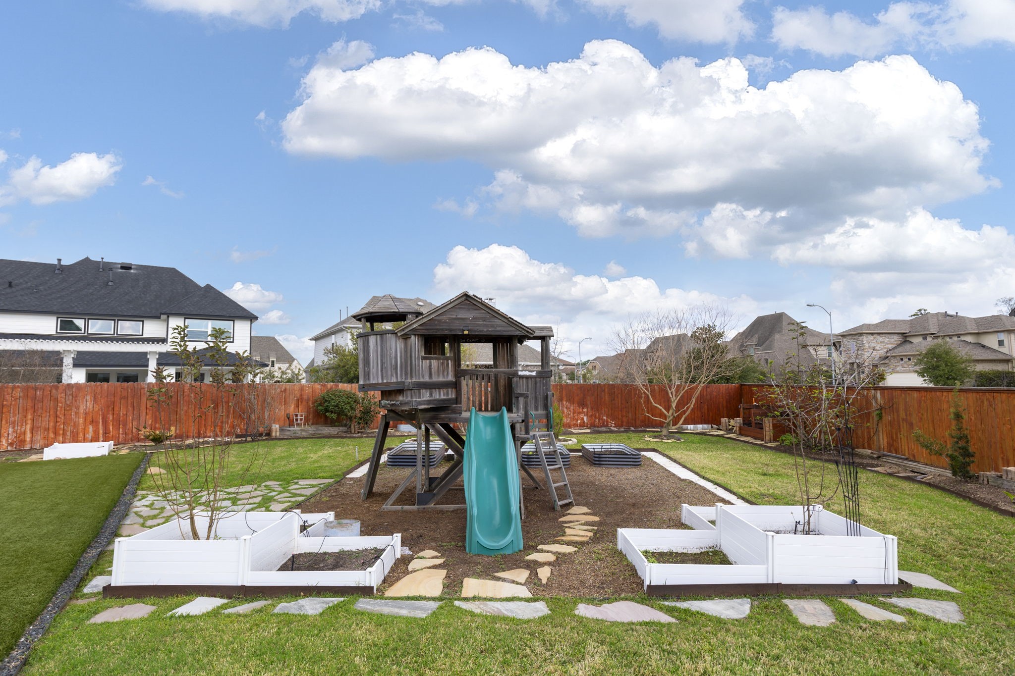 25002 Rosa Aurora Way Spring, TX 77389 - Photo 36 of 38 Spacious backyard featuring a wooden playset with a slide, surrounded by a well-maintained lawn and garden beds.