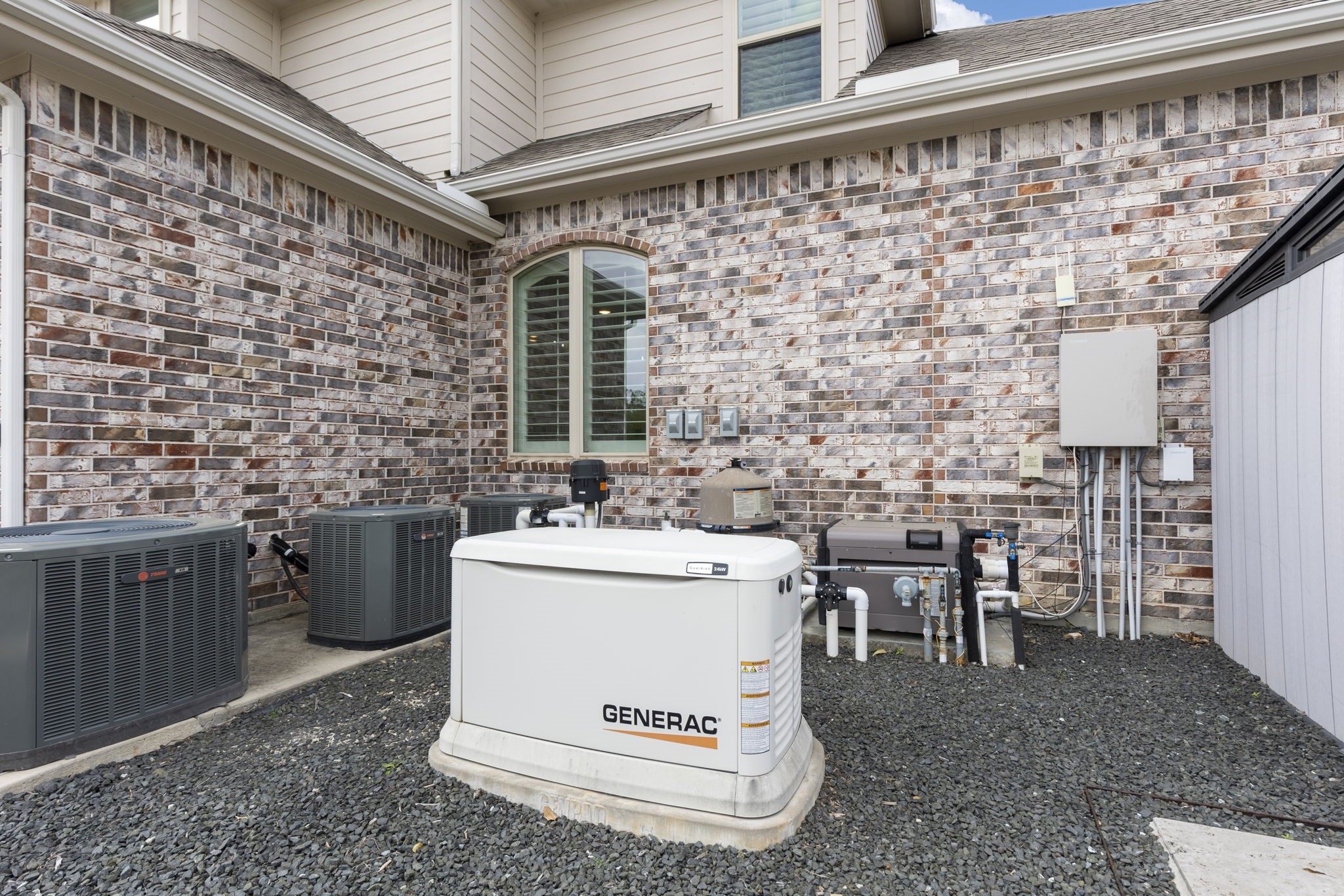 25002 Rosa Aurora Way Spring, TX 77389 - Photo 38 of 38 This photo shows the exterior utility area of a home with brick siding, featuring a Generac generator and multiple HVAC units, providing essential backup power and climate control solutions.