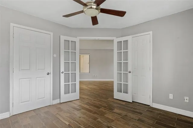 a view of an empty room with wooden floor and a ceiling fan