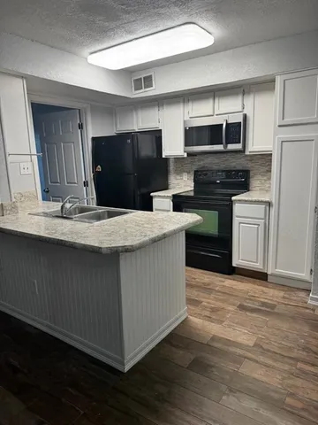 a kitchen with stainless steel appliances kitchen island granite countertop a stove a refrigerator a sink and dishwasher with wooden floor