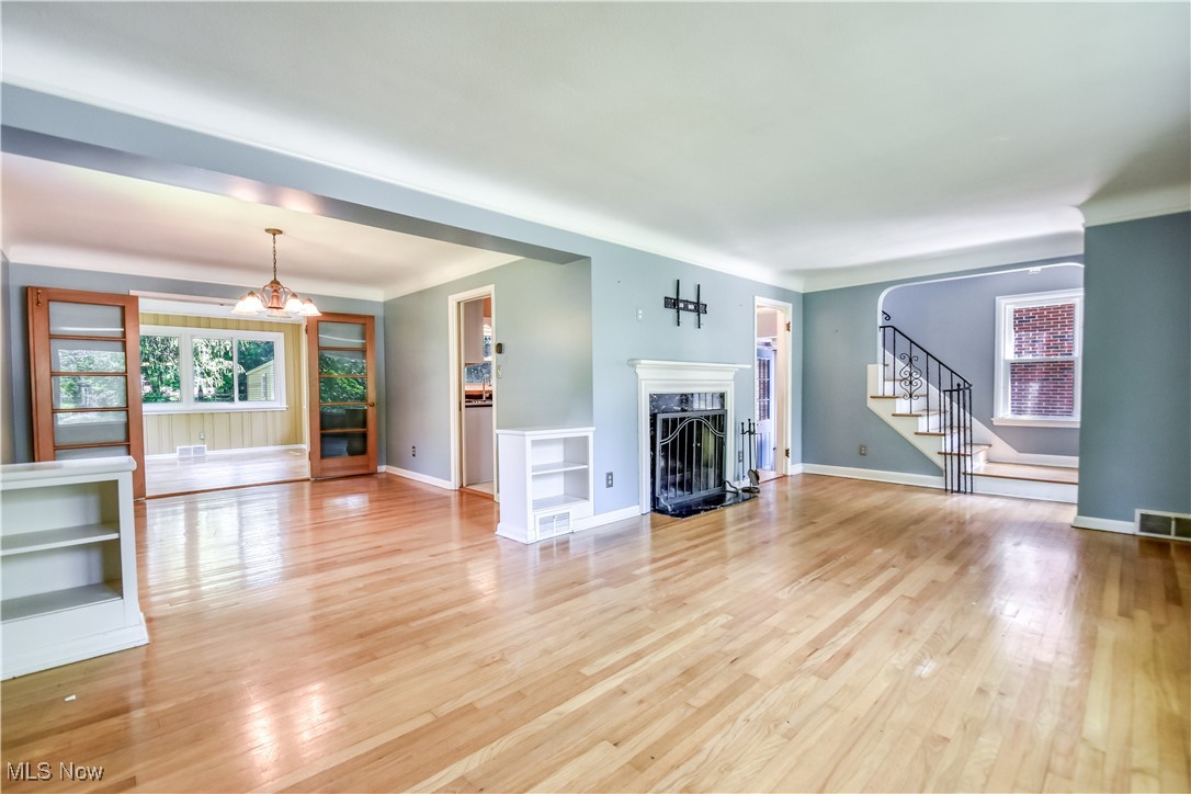 2607 Ashurst Road University Heights, OH 44118 - Photo 13 of 39 Unfurnished living room with stairs, light wood-type flooring, a premium fireplace, and a chandelier