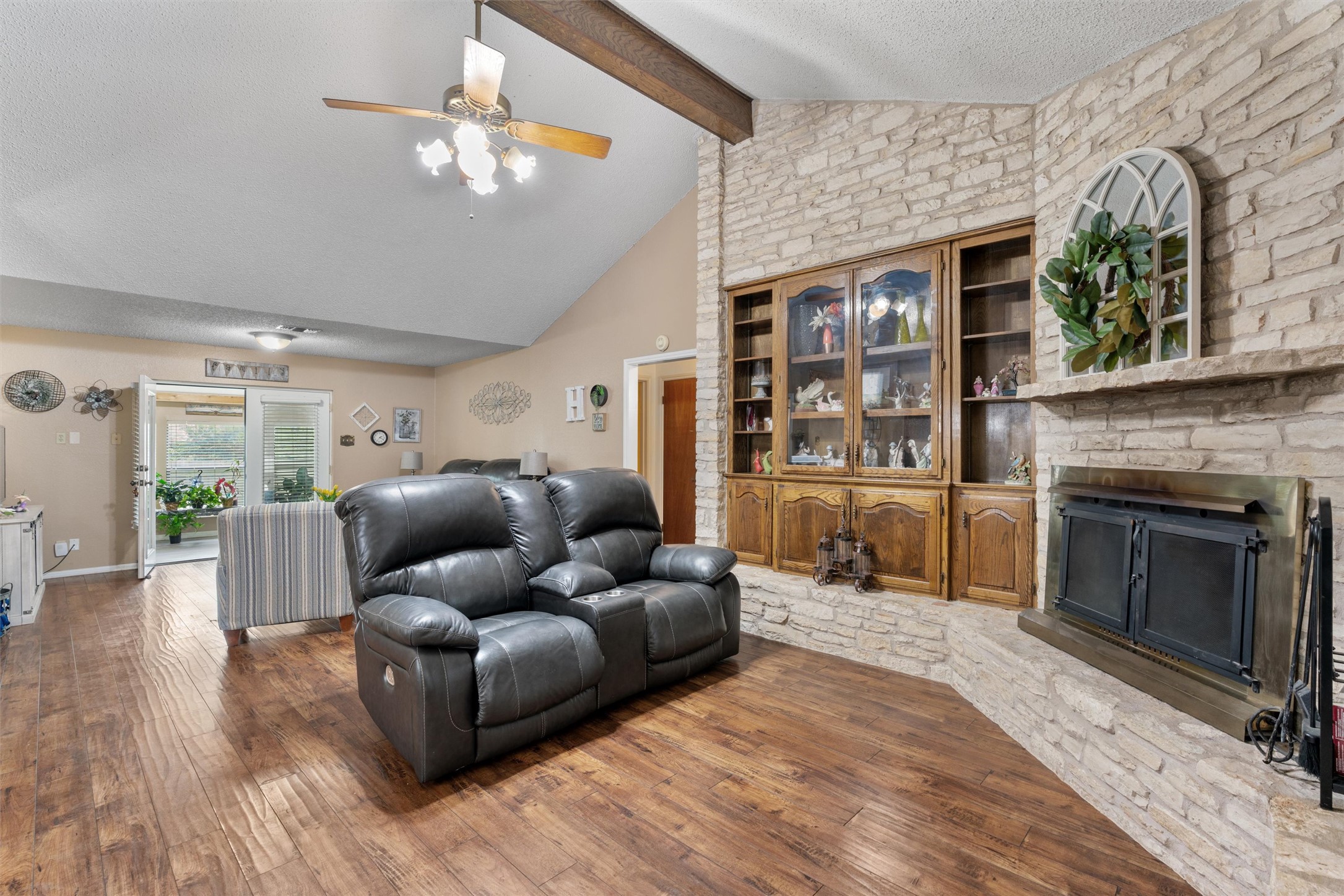 401 Drake Lane Taylor, TX 76574 - Photo 4 of 31 Living area featuring vaulted ceilings with exposed wood beams, wood-finish flooring, a stone accent wall, and a built-in wood display cabinet