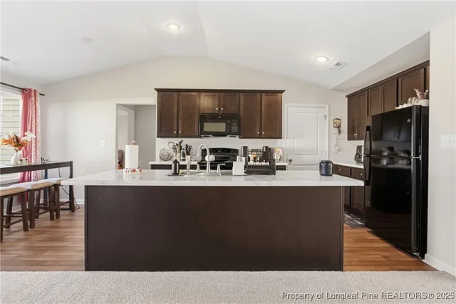 a kitchen with stainless steel appliances kitchen island granite countertop a refrigerator a stove a sink and a dining table with wooden floor