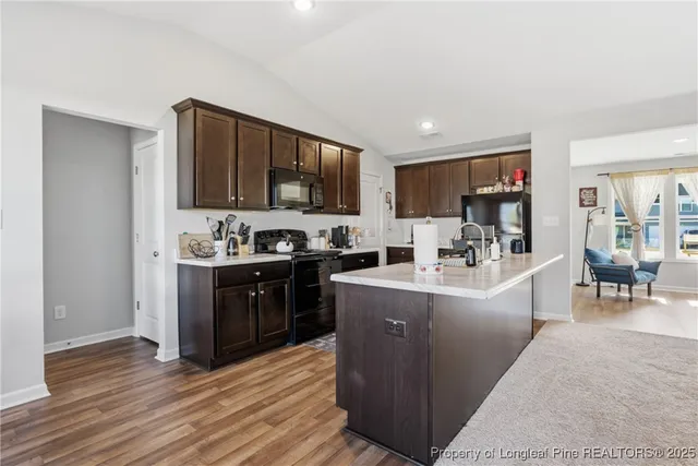 a living room with stainless steel appliances kitchen island granite countertop a refrigerator a stove top oven a sink and a dining table with wooden floor