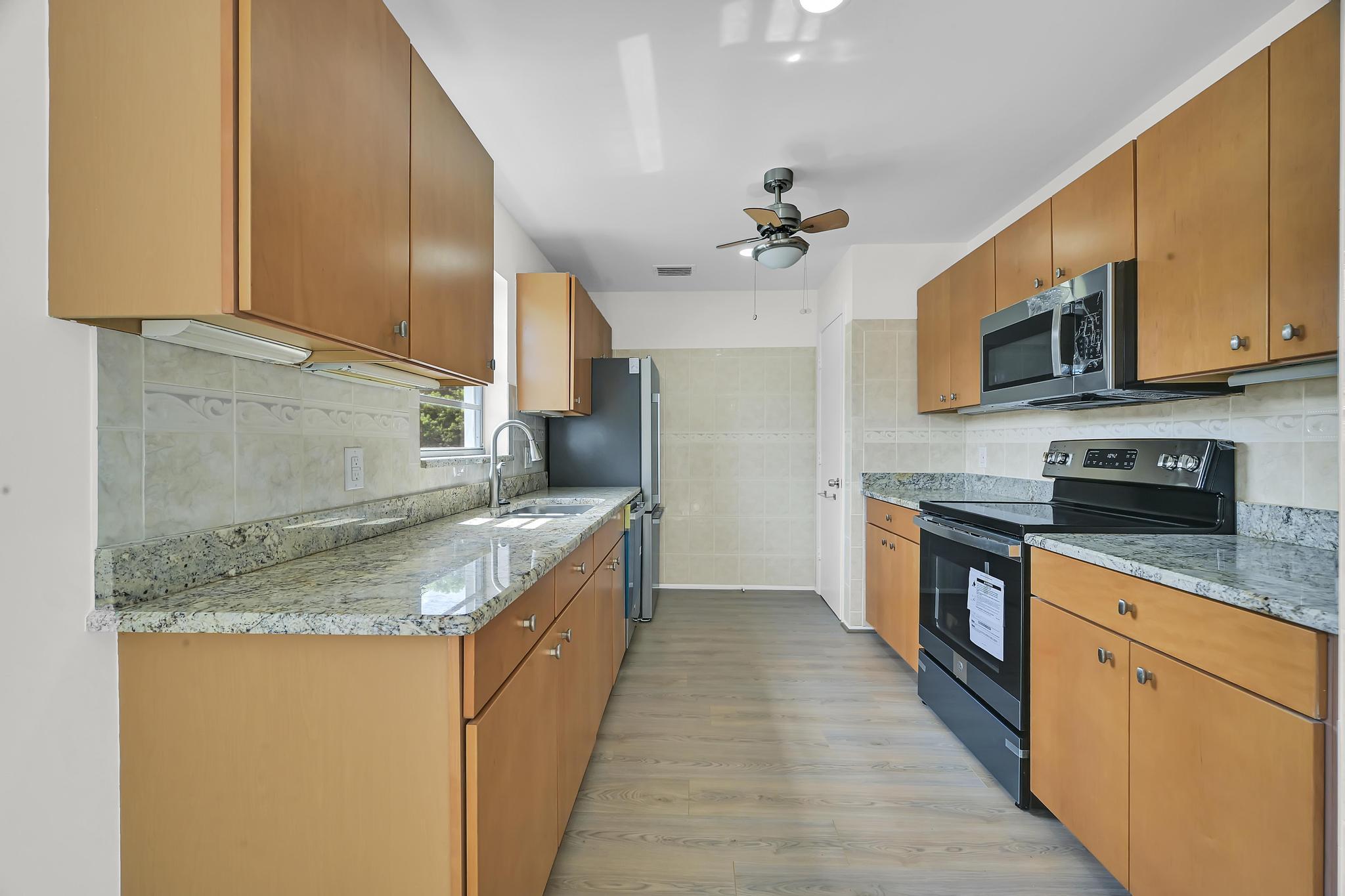 2 Lake Vista Trail, Unit 107 Port St. Lucie, FL 34952 - Photo 6 of 19 a kitchen with stainless steel appliances granite countertop a sink a stove top oven a refrigerator with wooden cabinets and floor