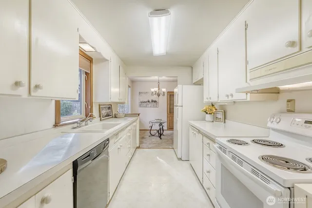 a large kitchen with a stove a sink dishwasher and white cabinets with wooden floor